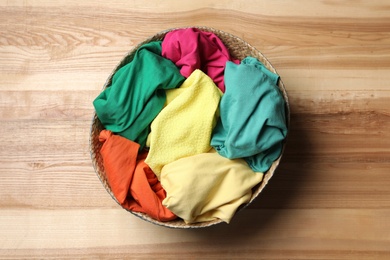 Photo of Wicker basket with laundry on wooden surface, top view