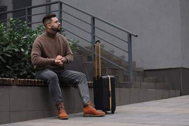 Photo of Being late. Worried man with suitcase sitting on bench outdoors, space for text