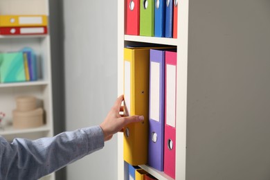 Photo of Woman taking binder office folder from shelving unit indoors, closeup