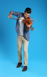 Happy man playing violin on light blue background