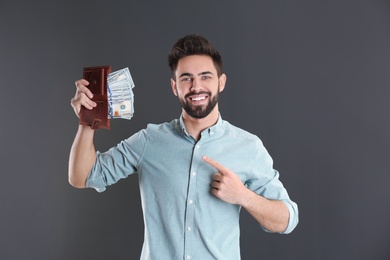 Photo of Happy young man with wallet full of money on grey background