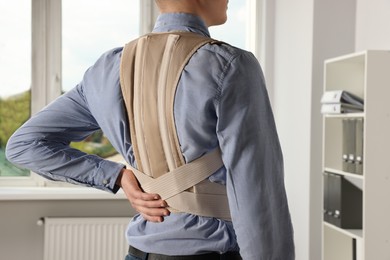 Photo of Closeup of man with orthopedic corset in room, back view