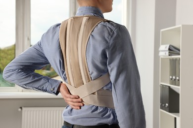 Closeup of man with orthopedic corset in room, back view