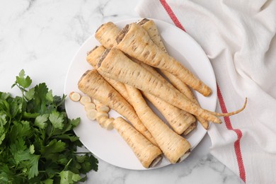 Photo of Raw parsley roots and fresh herb on white marble table, flat lay