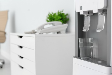 Photo of Modern water cooler with glass in office, closeup. Space for text