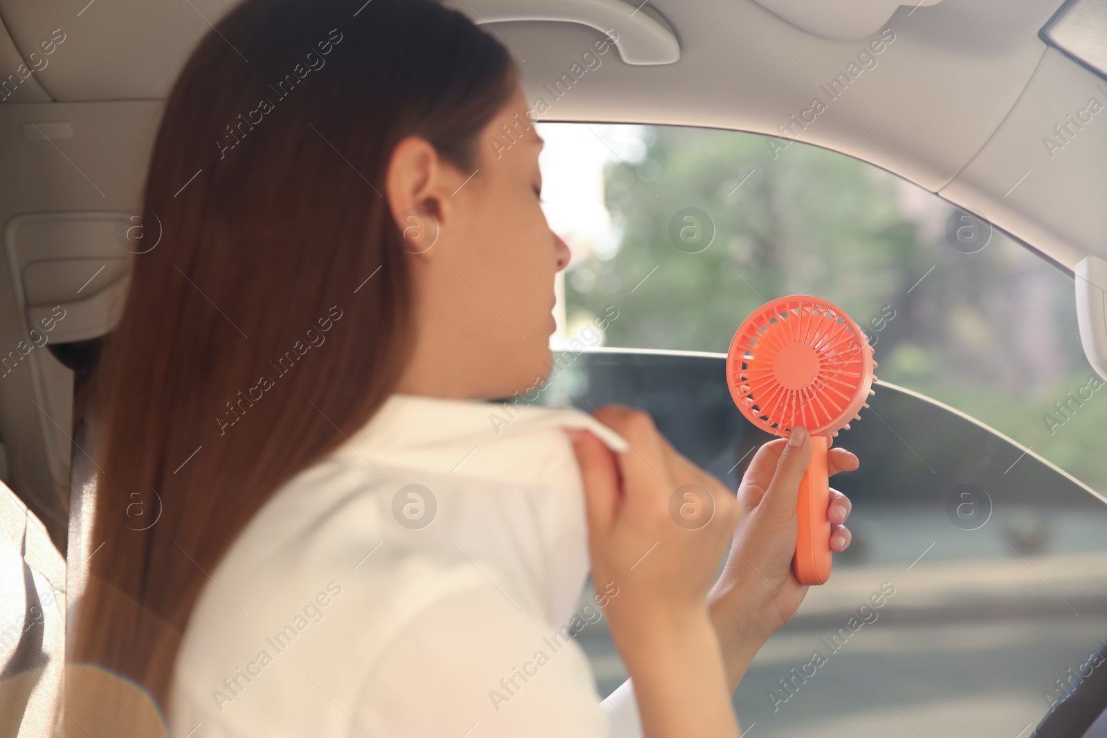 Photo of Young woman with portable fan suffering from heat in car on summer day