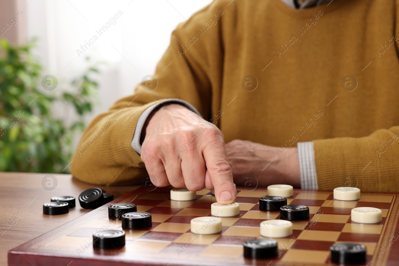 Photo of Playing checkers. Senior man thinking about next move at table in room, closeup