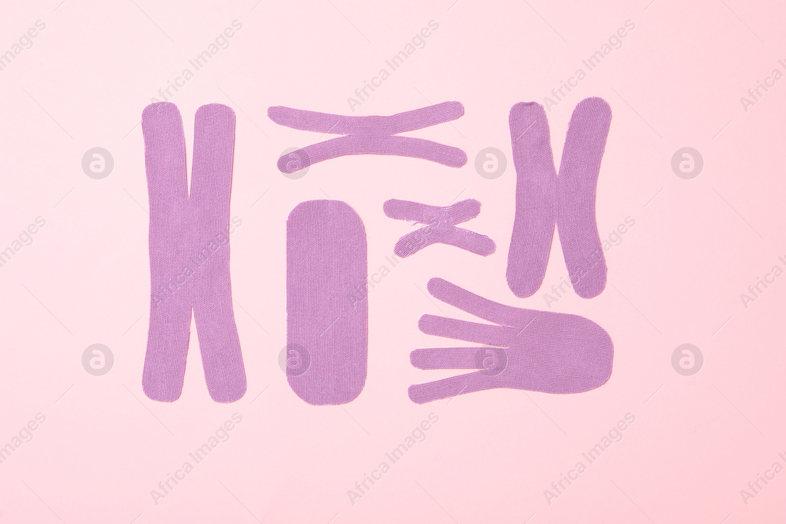 Photo of Violet kinesio tape pieces on light pink background, flat lay