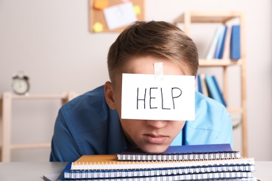 Young man with note HELP on forehead at workplace