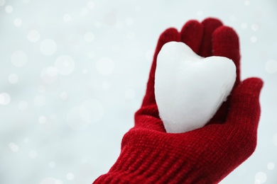 Photo of Woman holding heart shaped snowball in hand, closeup