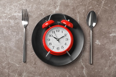 Flat lay composition with alarm clock, plate and utensils on grey background