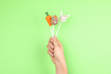 Photo of Woman with delicious cake pops on light green background, closeup. Easter holiday