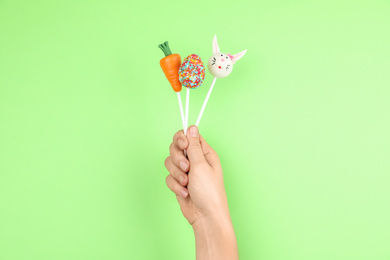 Woman with delicious cake pops on light green background, closeup. Easter holiday