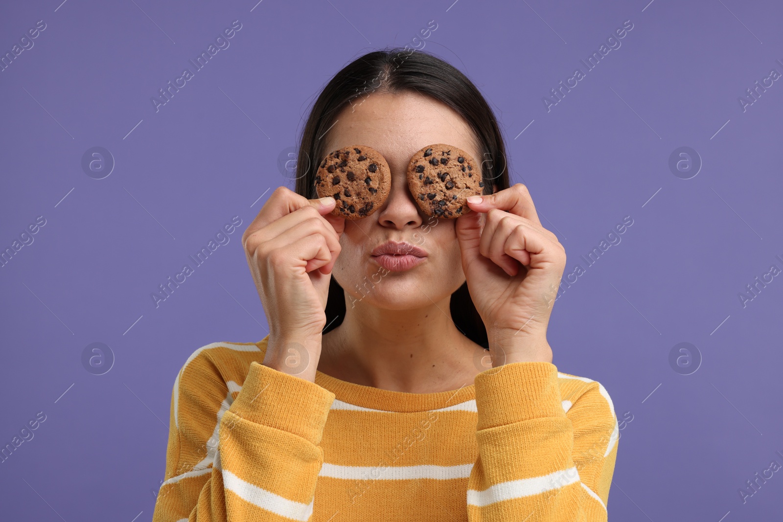 Photo of Young woman with chocolate chip cookies on purple background