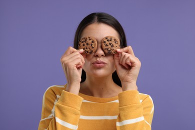 Young woman with chocolate chip cookies on purple background