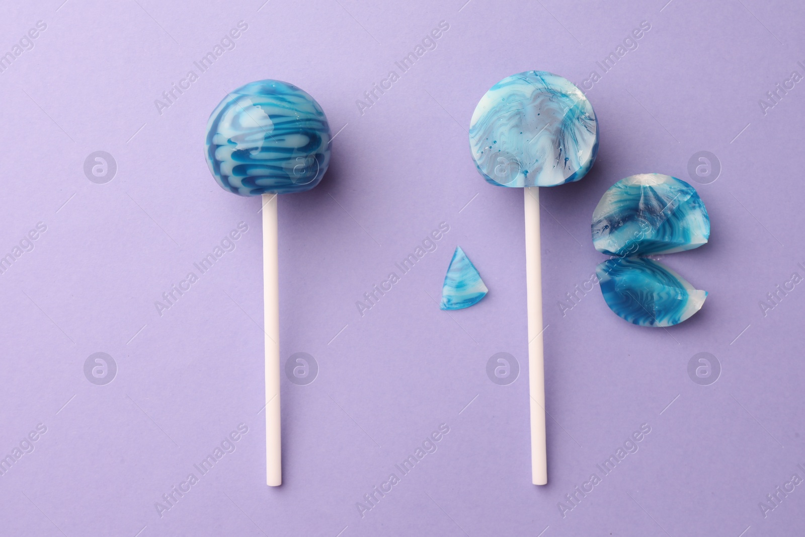 Photo of Whole and broken lollipops on violet background, flat lay