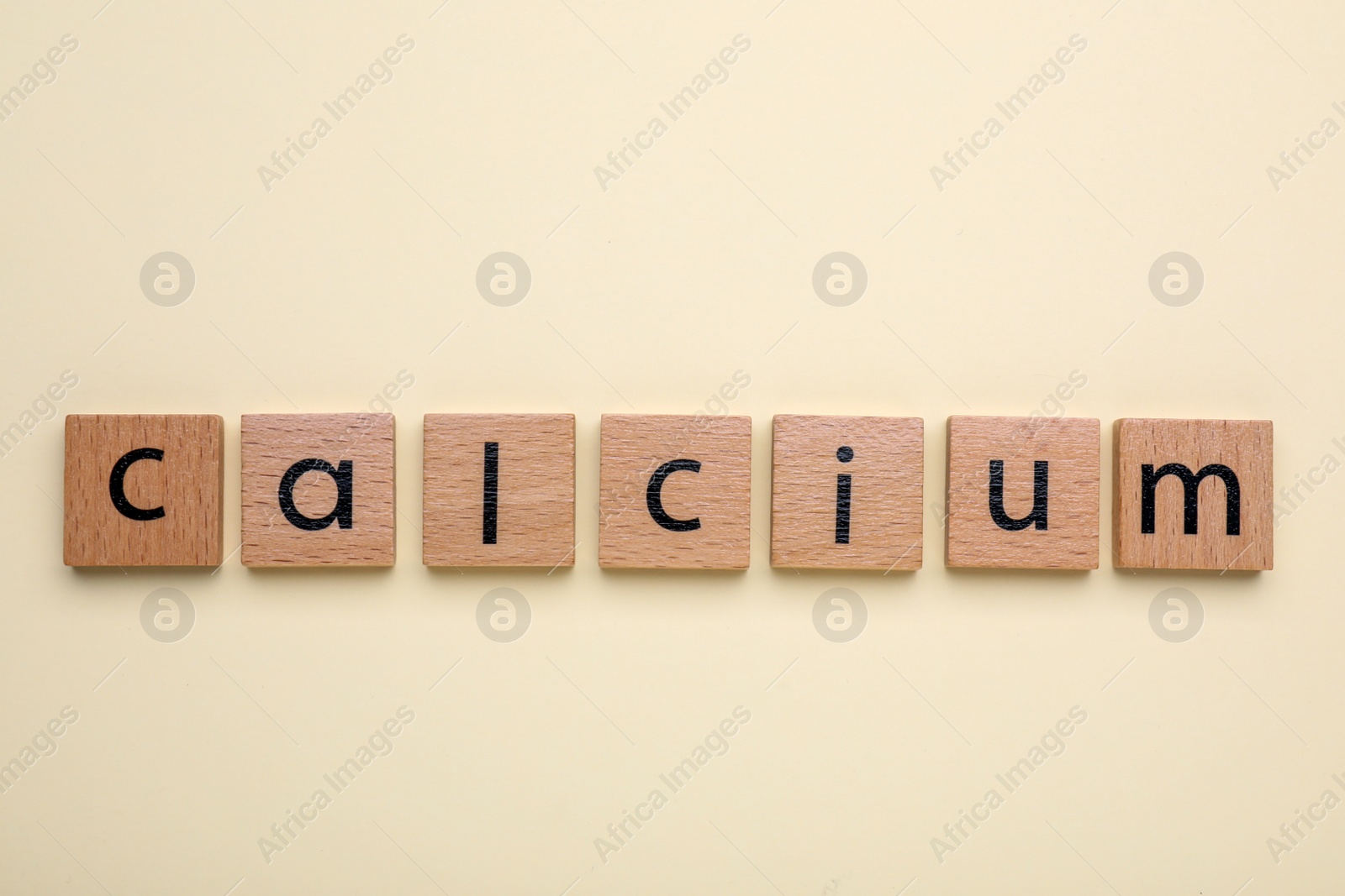 Photo of Word Calcium made of wooden cubes with letters on beige background, top view