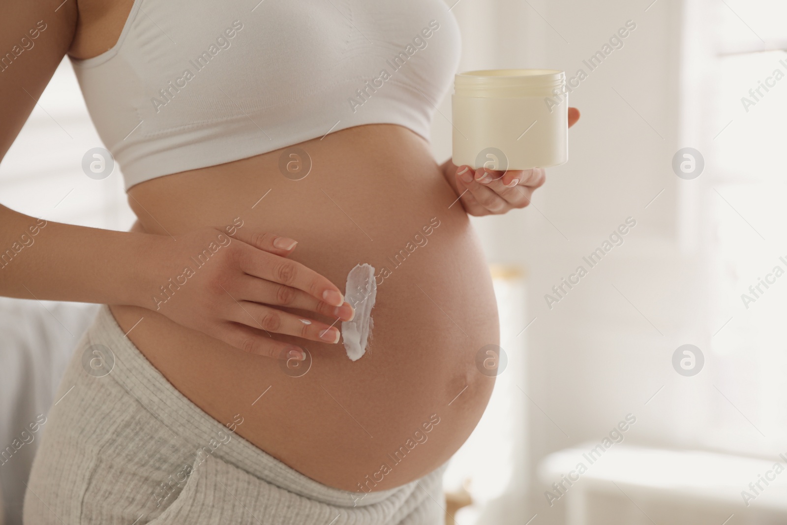 Photo of Young pregnant woman with cosmetic product indoors, closeup. Space for text