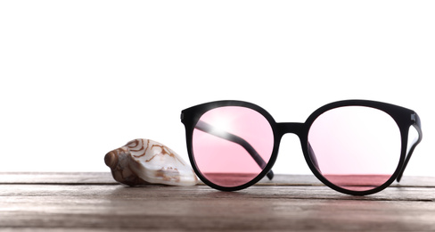 Photo of Stylish sunglasses and shell on wooden table against white background