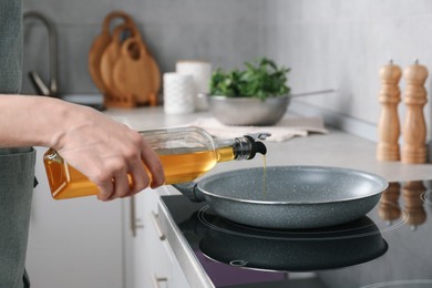 Photo of Vegetable fats. Woman pouring cooking oil into frying pan on stove in kitchen, closeup