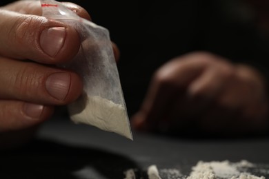 Photo of Addicted man with plastic bag of hard drug on blurred background, selective focus. Space for text