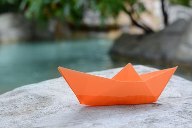 Photo of Beautiful orange paper boat on stone near pond, closeup