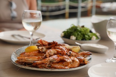 Photo of Plate of delicious cooked shrimps served with lemon and wine at table outdoors, closeup