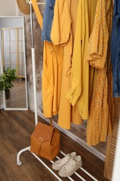 Different stylish clothes hanging on rack in room