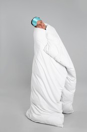 Man in mask wrapped with blanket sleeping on grey background