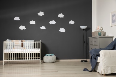 Cute baby room interior with modern crib near decorative clouds on dark wall
