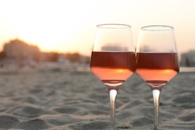 Glasses of tasty rose wine on sandy beach, space for text