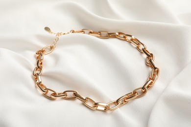 Photo of Elegant golden necklace on white fabric. Stylish bijouterie