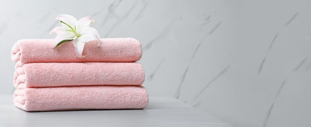Image of Stack of folded pink towels with white lily on table against light background, space for text. Banner design