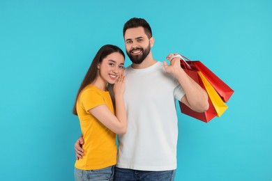 Happy couple with shopping bags on light blue background