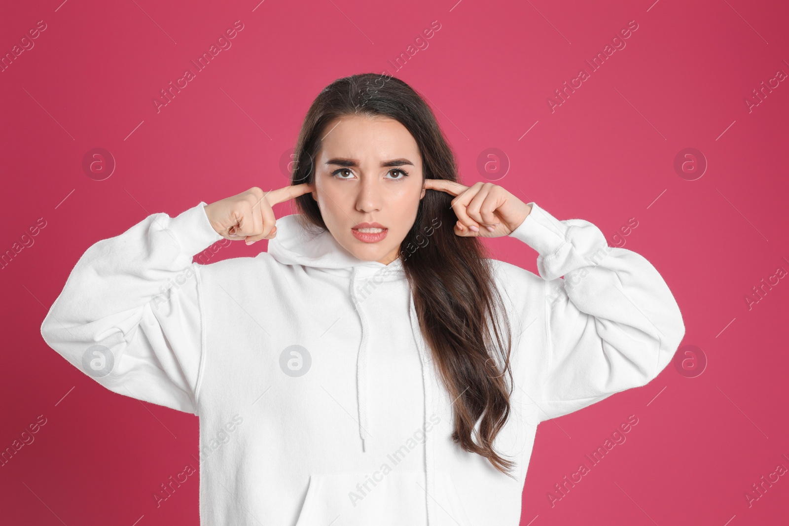 Photo of Young woman covering ears with fingers on pink background