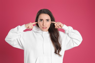 Young woman covering ears with fingers on pink background