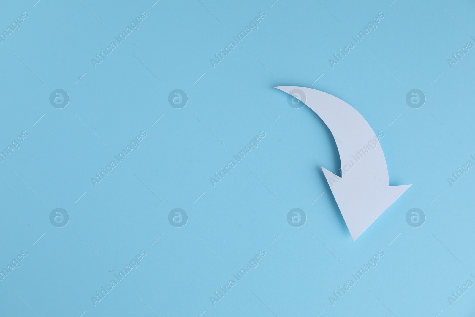 Photo of White curved paper arrow on light blue background, top view. Space for text