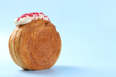 Photo of One supreme croissant with cream on light blue background, closeup with space for text. Tasty puff pastry