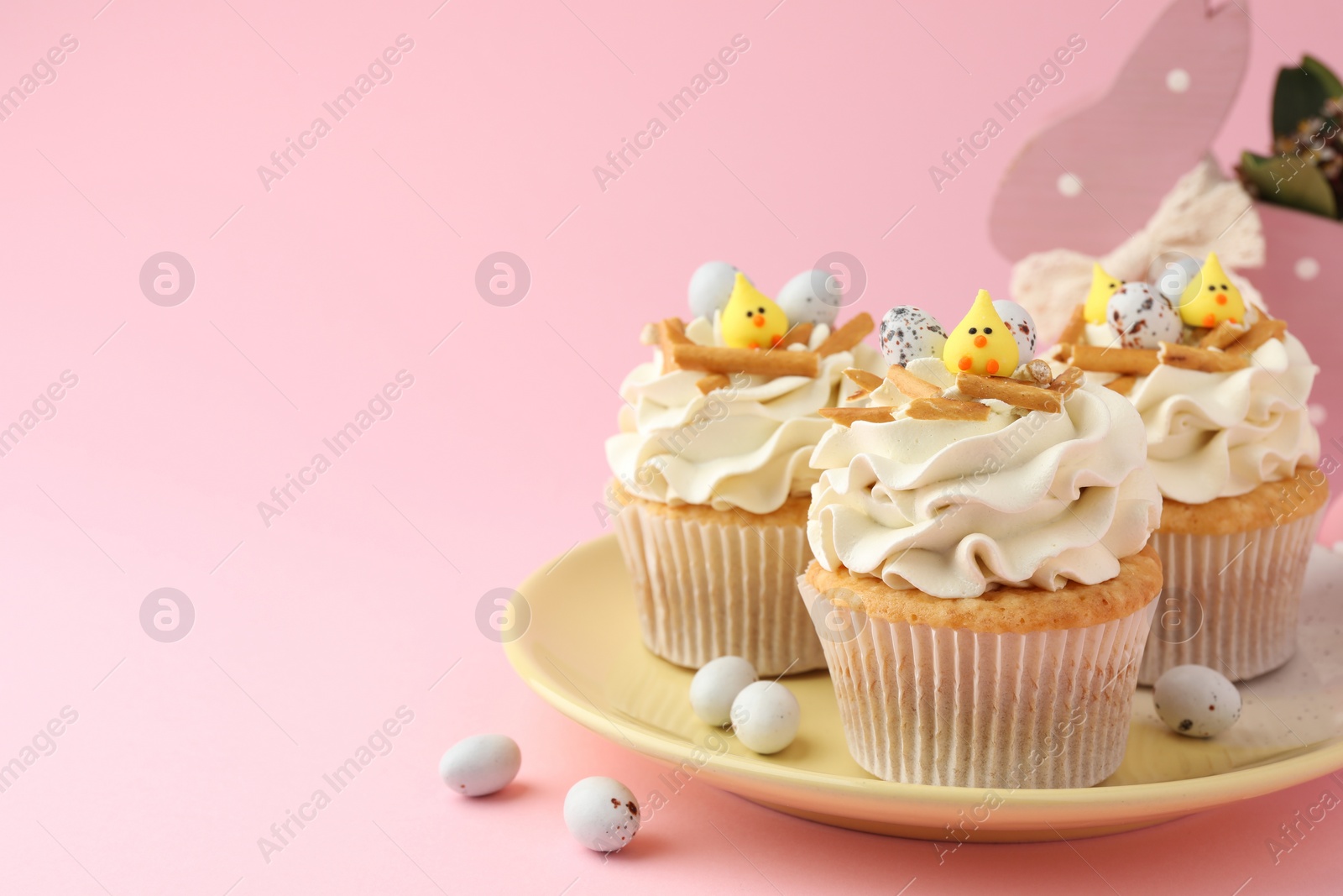 Photo of Tasty Easter cupcakes with vanilla cream and candies on pink background, space for text