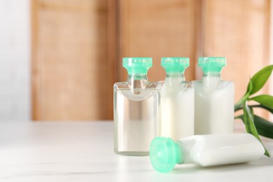 Photo of Mini bottles of cosmetic products and green branch on white table against blurred background. Space for text