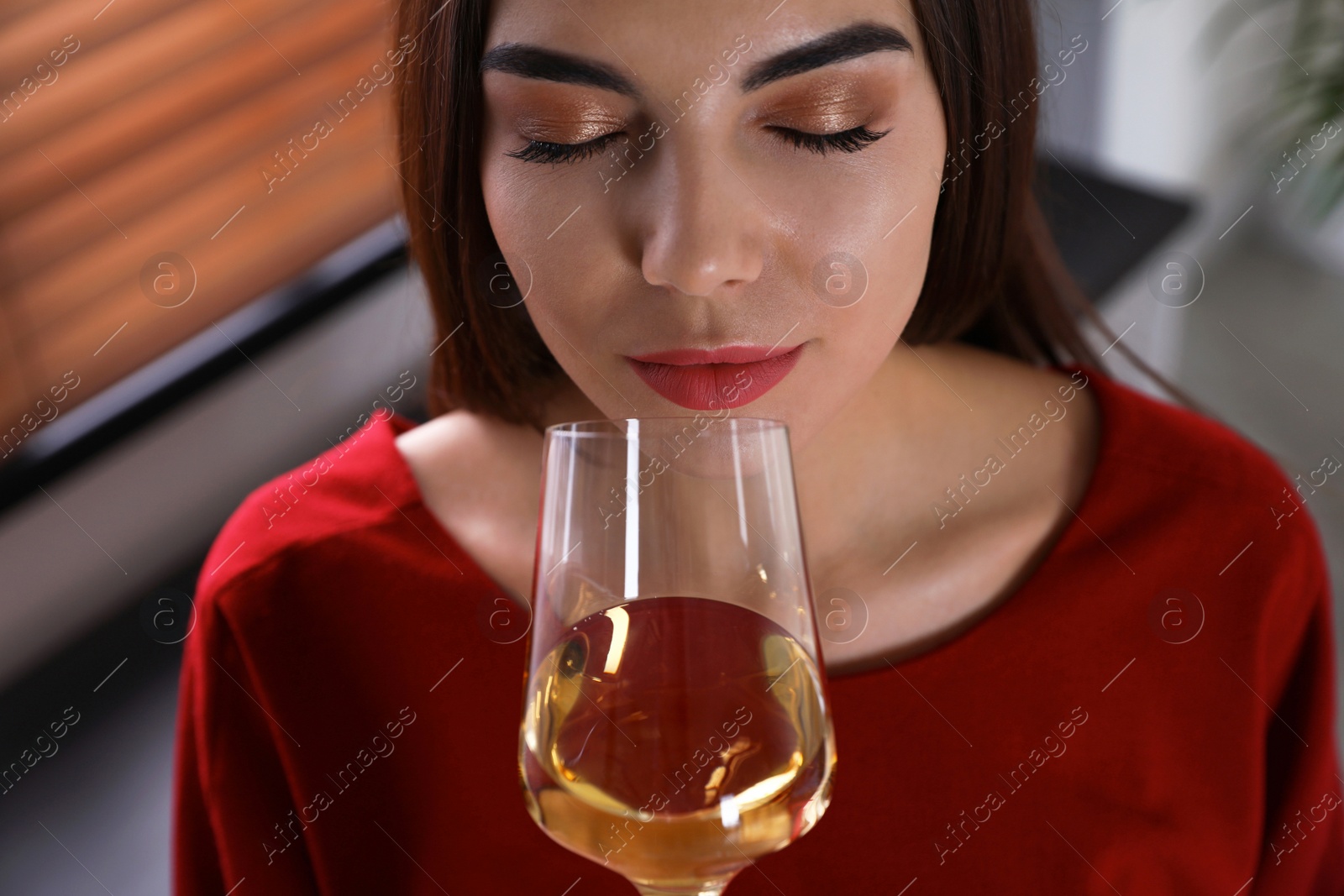 Photo of Beautiful young woman with glass of luxury white wine indoors, closeup view