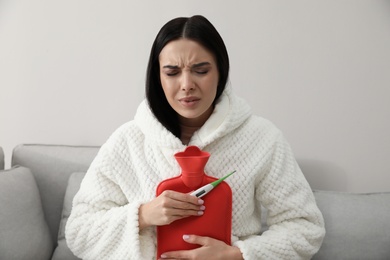 Photo of Ill woman with hot water bottle checking her temperature at home