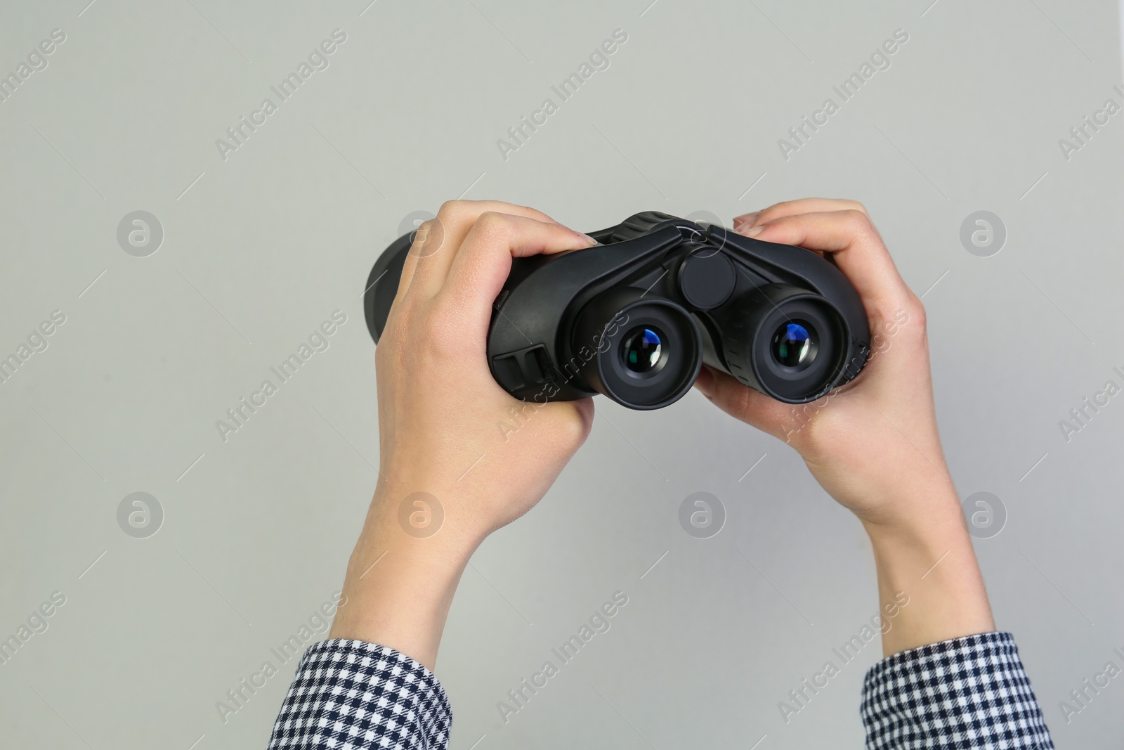 Photo of Woman holding modern binoculars on grey background, closeup