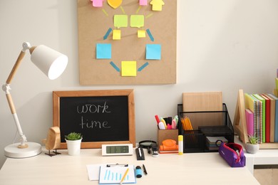 Business process planning and optimization. Workplace with lamp, small blackboard, colorful paper notes and other stationery on white wooden table