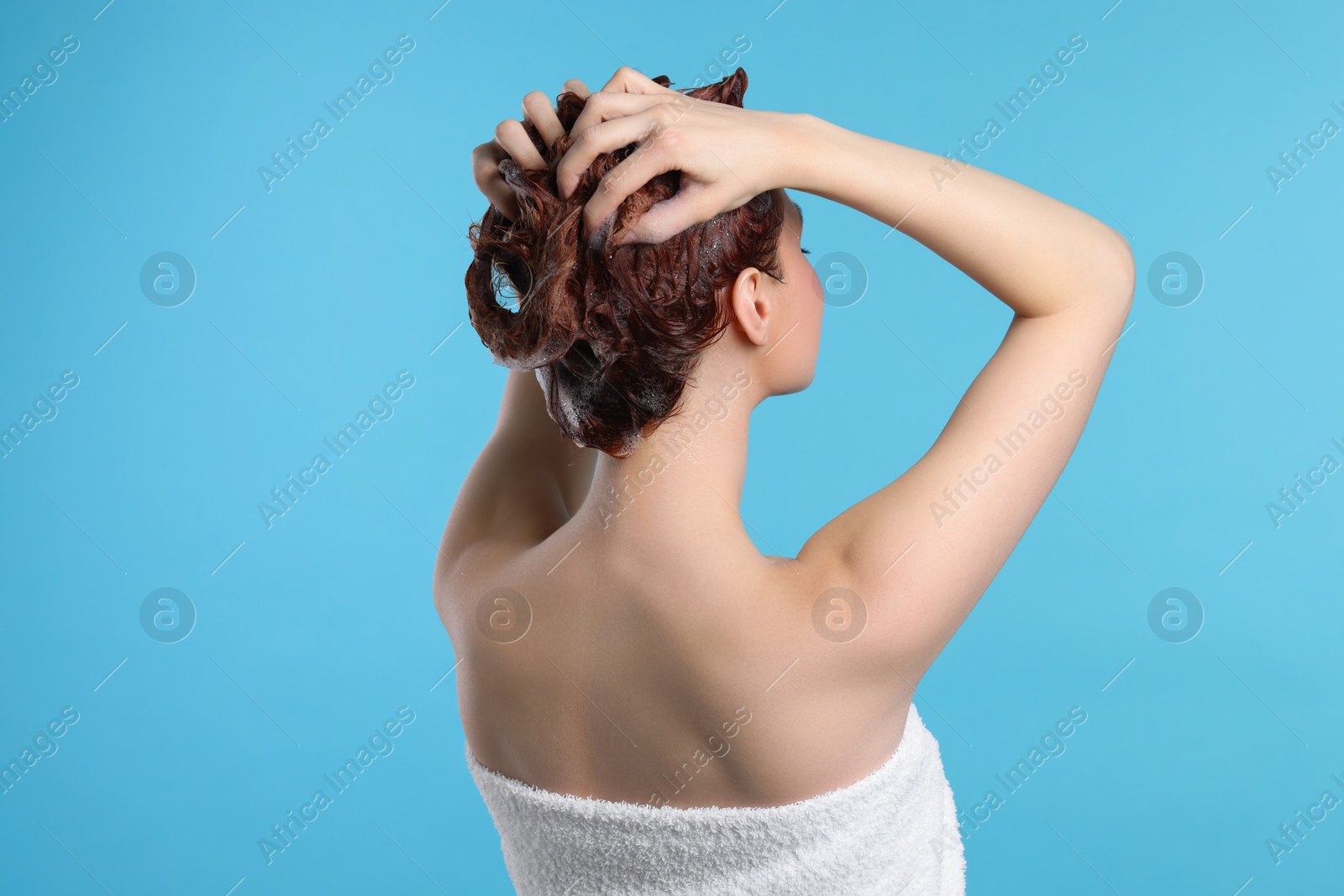 Photo of Young woman washing her hair with shampoo on light blue background, back view