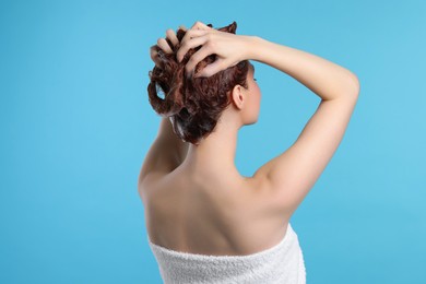 Photo of Young woman washing her hair with shampoo on light blue background, back view