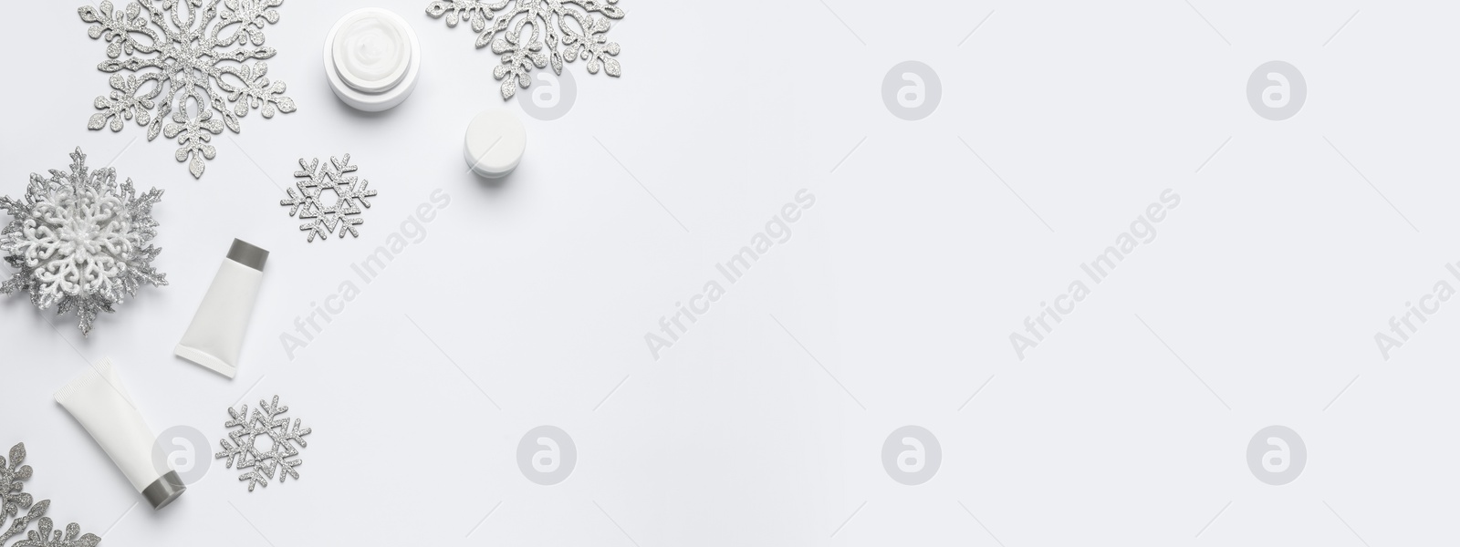 Image of Winter skin care. Composition with cosmetic products and snowflakes on white background, top view. Banner design