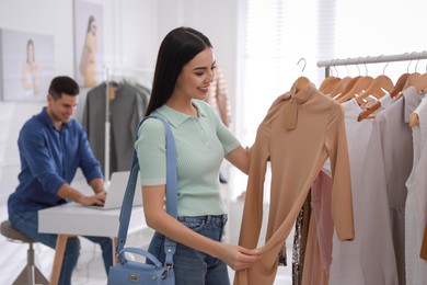 Photo of Young woman choosing clothes near rack in modern boutique