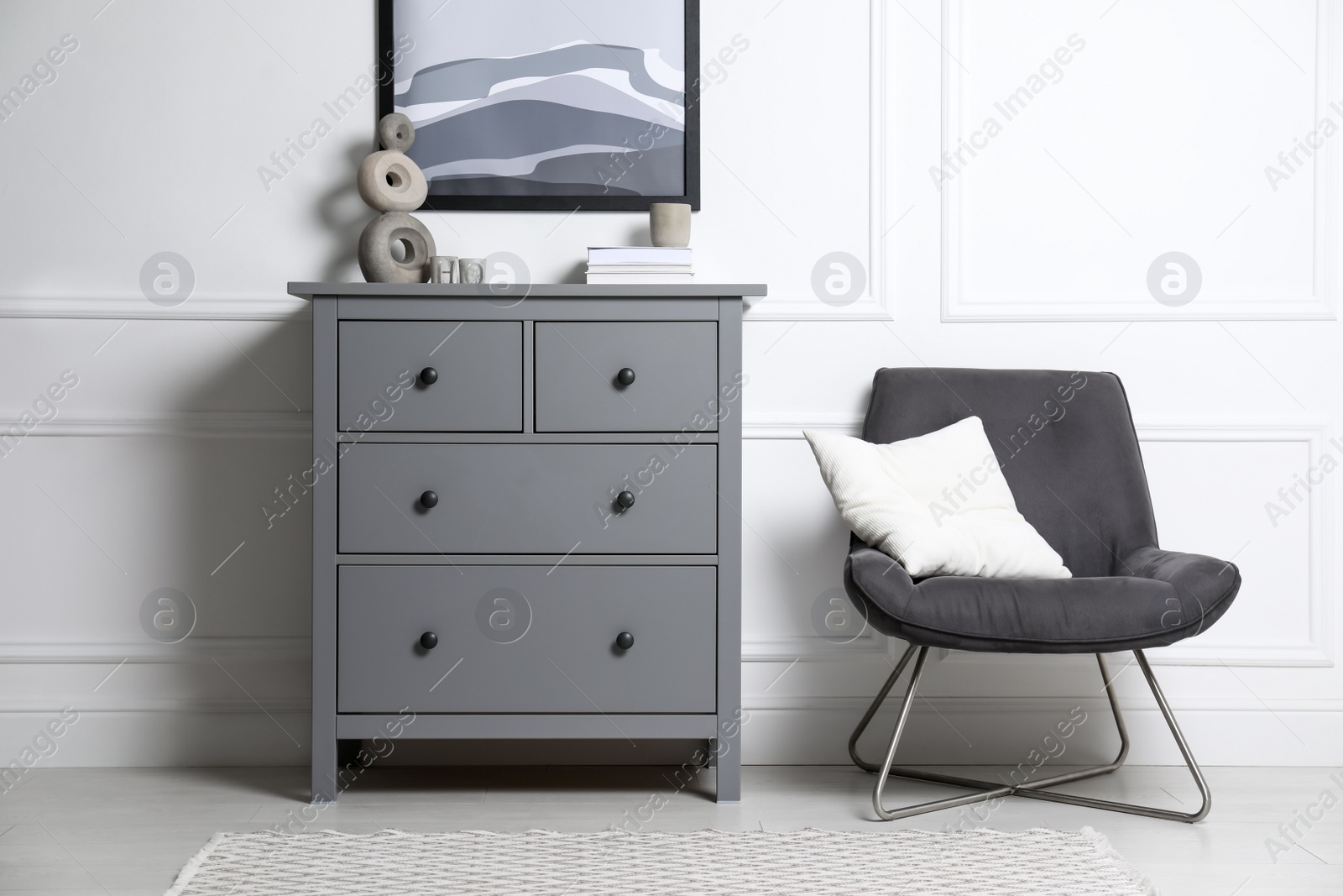 Photo of Stylish room interior with grey chest of drawers and comfortable chair