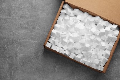 Photo of Cardboard box filled with polystyrene styrofoam pieces on grey background, top view. Space for text